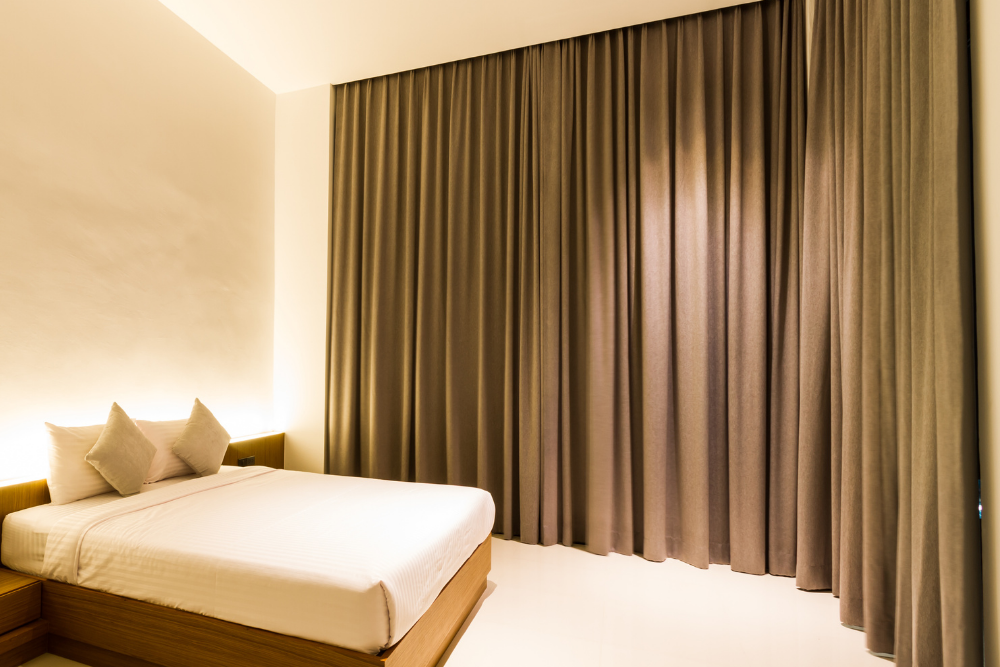 A minimalist bedroom with a wooden bed, white bedding, and floor-to-ceiling brown curtains, showcasing sophisticated home furnishing.