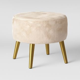 Beige upholstered ottoman with golden legs, a stylish home furnishing piece designed to add comfort, elegance, and modern charm to interiors.